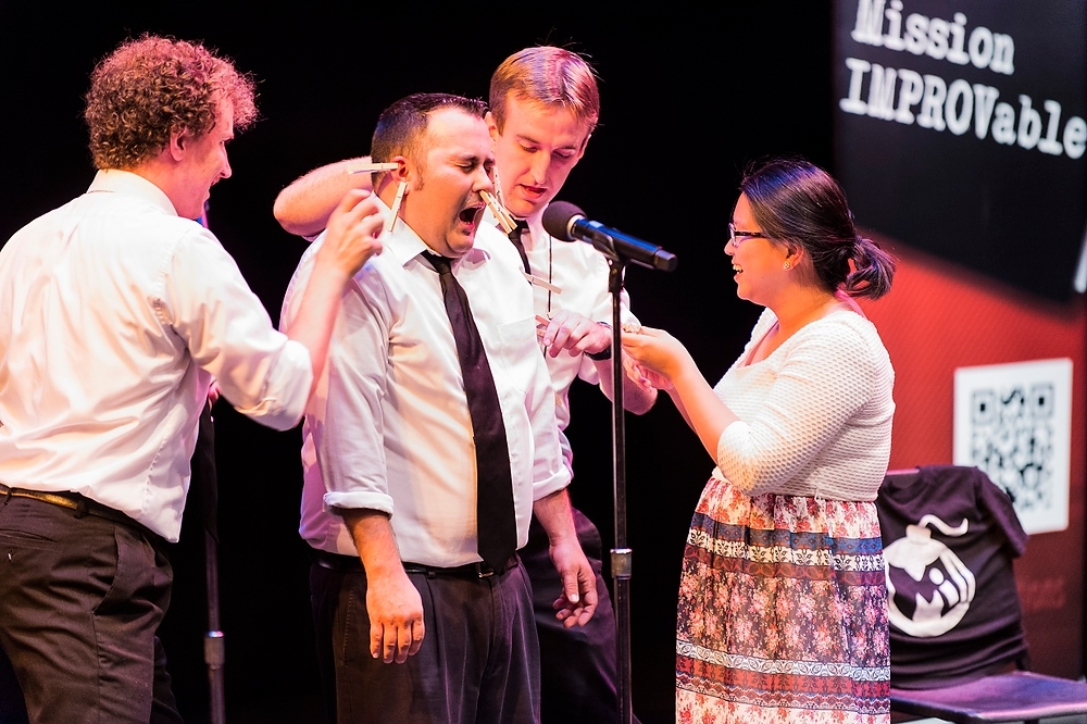 Photo: A losing comedian endure the application of clothes pins during comedy show by Mission IMPROVable.