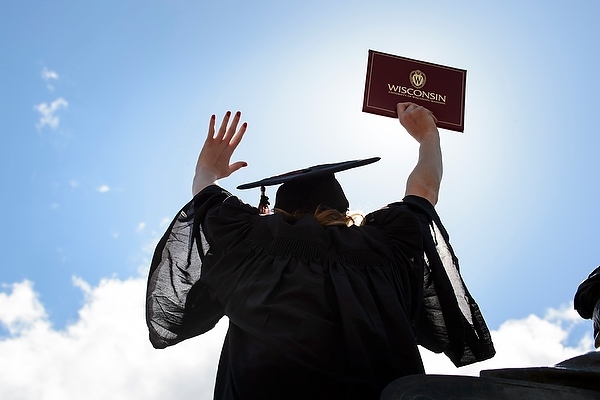 Photo: Graduate with arms outstretched toward sky holding diploma