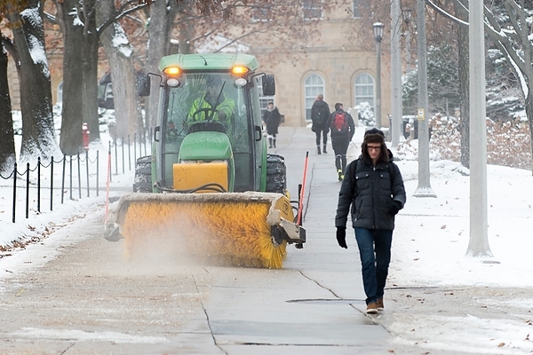 Photo: A member of the UW grounds crew drives a tractor with brush sweeper to clear the sidewalk of snow as pedestrian walk along Bascom Hill at the University of Wisconsin–Madison during winter on Nov. 25, 2014
