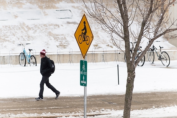Photo: A pedestrian walks past parked bicycles and a bike route sign near the Mosse Humanities Building
