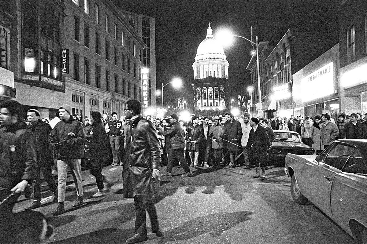 Wide shot of a large march led by African American campus leaders at night on State Street with the Wisconsin State Capitol in the background. Photo by John Wolf