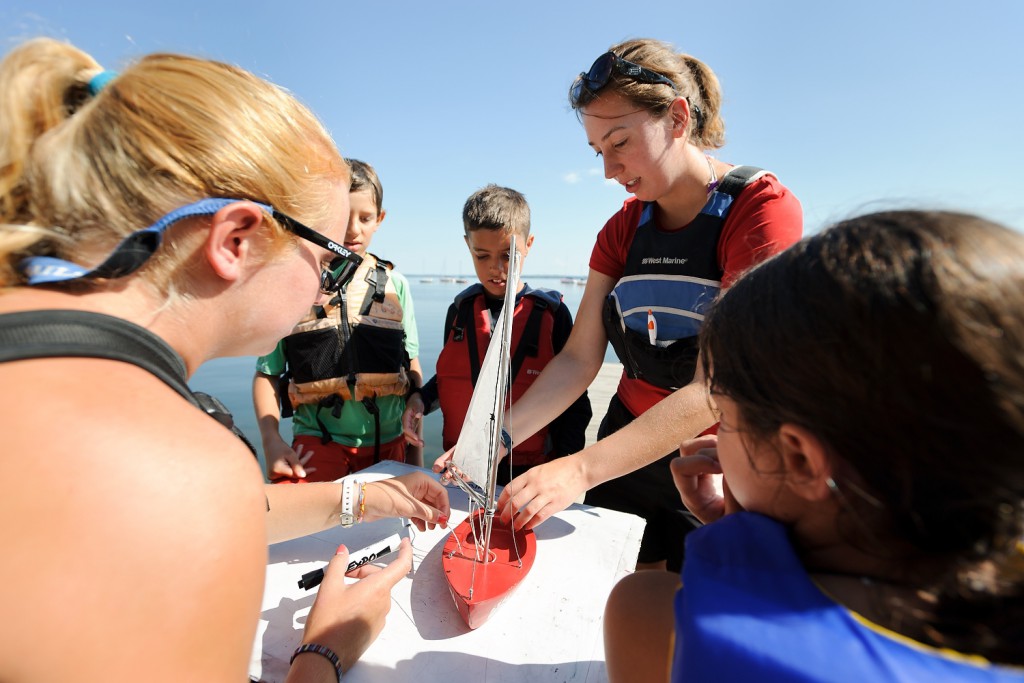 Using a miniature replica, undergraduate student instructors Katlyn Putney, left, and Ella Stutz, center, teach sailboat maneuvers during a "ground school" portion of a Hoofer Youth Sailing program near Lake Mendota.