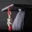 Closeup of a black mortarboard hat with a red tassel adorned with a Bucky Badger charm