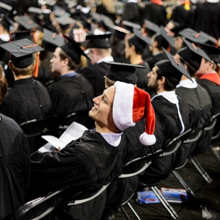 A graduate wearing a Santa hat adds a pop of color amid a sea of black caps and gowns.