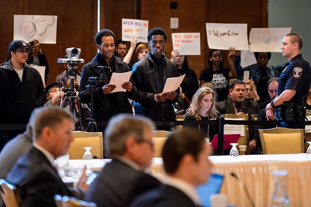 More than 50 people aligned with the Black Lives Matter Movement, including UW–Madison student Tyriek Mack (center of photo), hold signs of protest, voice their concerns about racial inequity on UW System campuses and briefly disrupt a UW System Board of Regents meeting on Feb. 5, 2016.