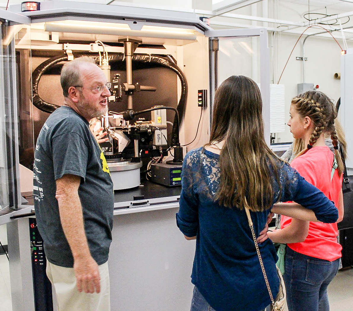 Darya Pronina of Waunakee Middle School and a friend look on as Dan Frankel, from the scientific instrument maker Bruker Corp., demonstrates a single-crystal X-ray diffractometer in the UW–Madison Chemistry Department. (Photo by Libby Dowdall)