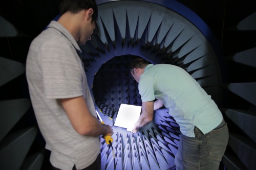 Photo: Amin Momeni illuminates the antenna-testing chamber while Nader Behdad installs a phased-array antenna. The flat surface consists of multiple precisely-positioned elements that convert spherical radio signals into single-column beams.