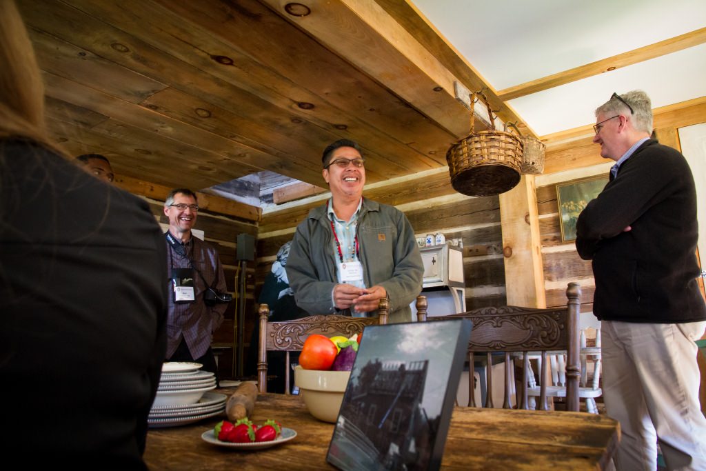 Kirby Metoxen, the Oneida Nation’s Special Events Tourism Coordinator, leads the Wisconsin Idea Seminar participants on a tour of Salt Pork Avenue, a cultural heritage site that features period homes representing various points in the Oneida Nation’s history in Wisconsin. Here Mr. Metoxen stands in the Tilly and Chancey Baird House, the former home of his grandparents (a life-size photo of his grandmother is just visible beyond his right elbow). 