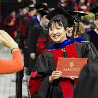 A graduate holds up her diploma cover to show family during UW-Madison's spring commencement ceremony at the Kohl Center at the University of Wisconsin-Madison on May 12, 2017. The indoor graduation was attended by approximately 830 doctoral, MFA and medical student degree candidates, plus their guests. (Photo by Bryce Richter / UW-Madison)