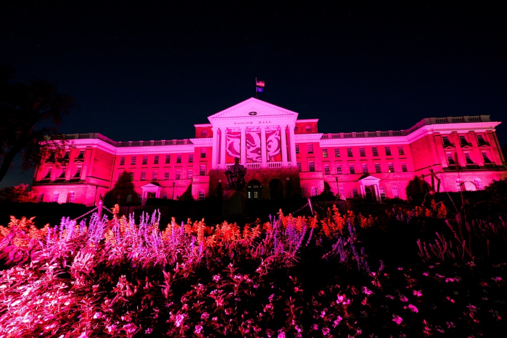 In honor of Breast Cancer Awareness Month, pink-colored accent lighting illuminates the exterior of Bascom Hall and terrace plantings surrounding the Abraham Lincoln statue at the University of Wisconsin-Madison as dawn brightens the night sky on Oct. 20, 2017. Hanging between the building's column is a graphic banner of UW-Madison mascot Bucky Badger. (Photo by Jeff Miller / UW-Madison)