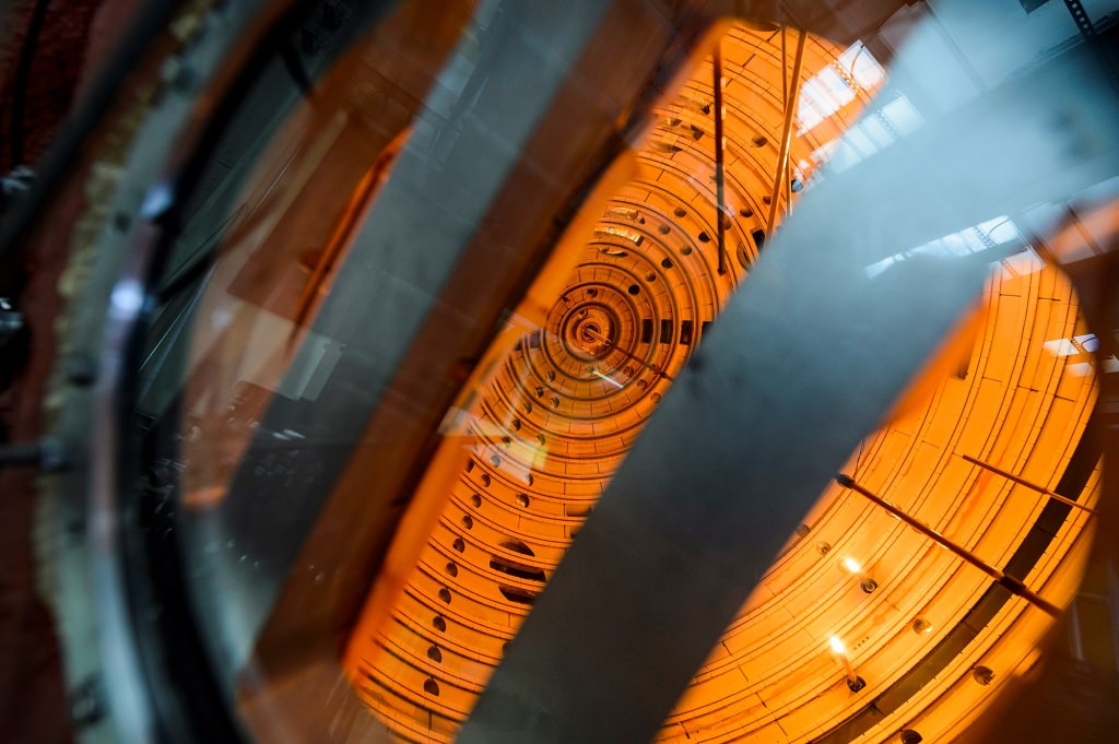 A look inside the fusion energy device known as the Big Red Ball. There are silver metal parts in the foreground against an orange background that appear to glow with energy. 