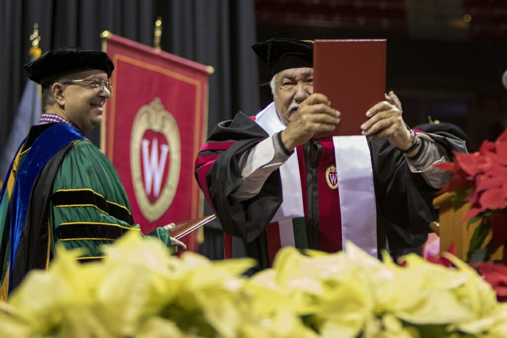 Photo of the graduate proudly displaying his diploma.