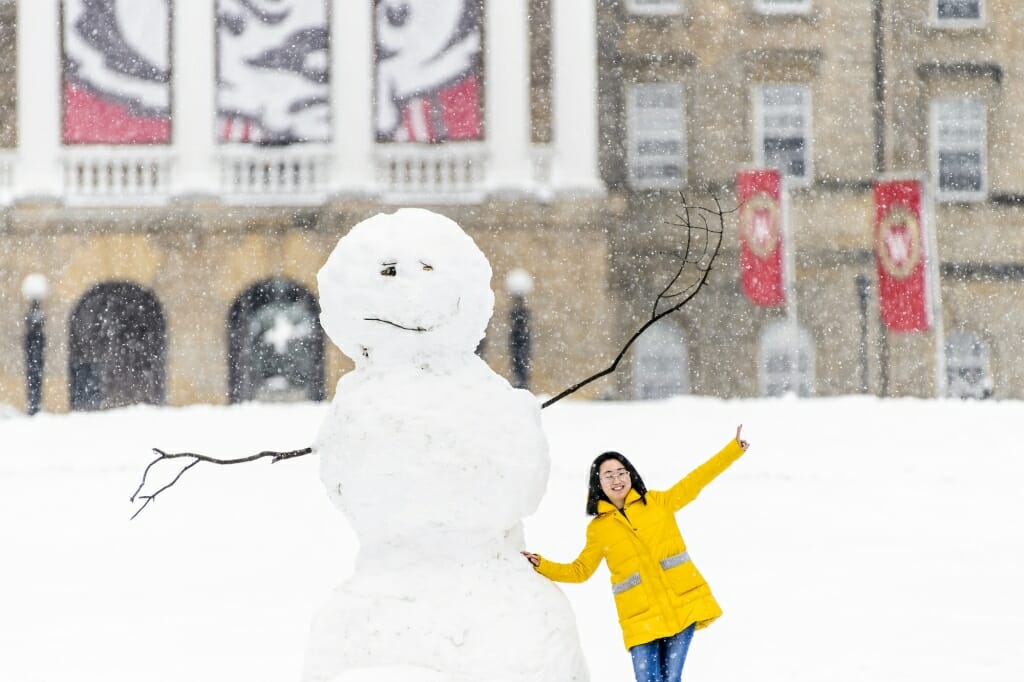 A student takes a photo with a snowman near the base of Bascom Hill.