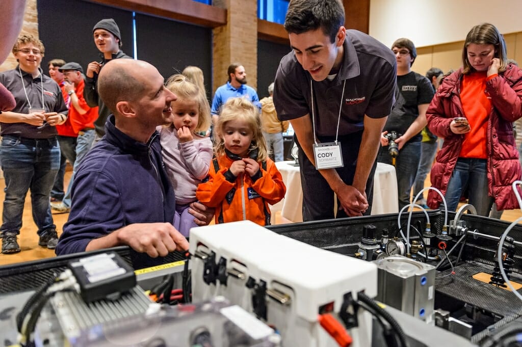 From left to right, Tom Stendel and his daughters Hailey and Madeline, 4.5 and dressed as an astronaut, talk with Badgerloop structural team lead Cody Schwartz as the Badgerloop team reveals their group's in-progress design for Badgerloop Pod III at Varsity Hall in Union South.