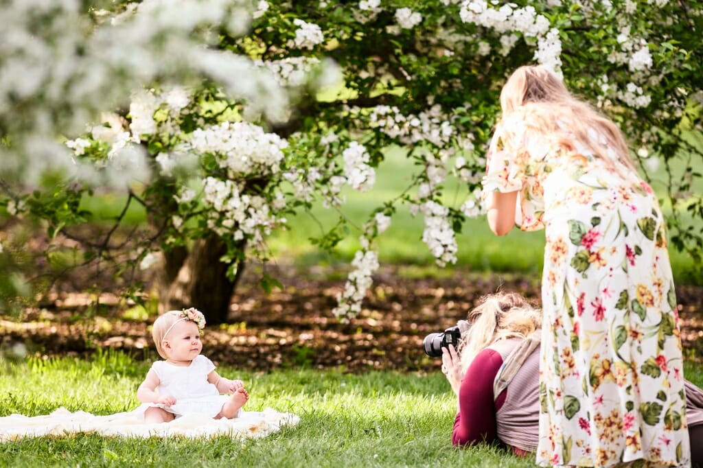 Photo: Person taking a picture of a baby sitting in front of a tree