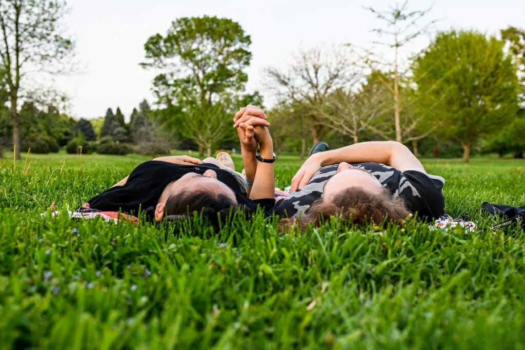 Photo: Couple holding hands lying on grass, looking up at sky