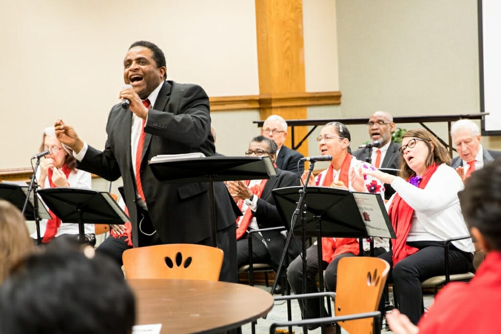 Photo: K.C. Williams singing into a microphone with people playing instruments