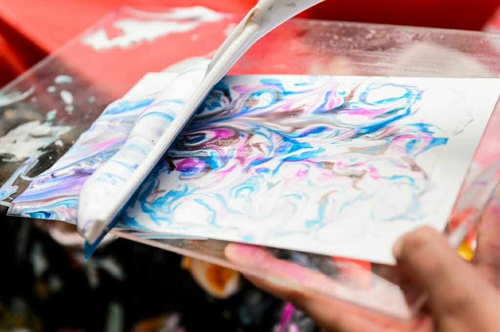 A volunteer squeegees away colored-shaving cream to reveal a patterned-paper print.