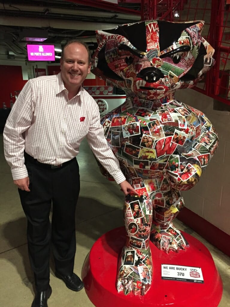 Men's Basketball Coach Greg Gard points to a postcard of himself on "We Are Bucky" at an unveiling event. 