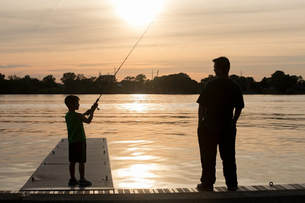 Photo: A boy casts a line into a lake as a man watches.