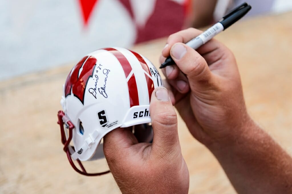 A player's large hands  dwarf a novelty helmet as he signs it.