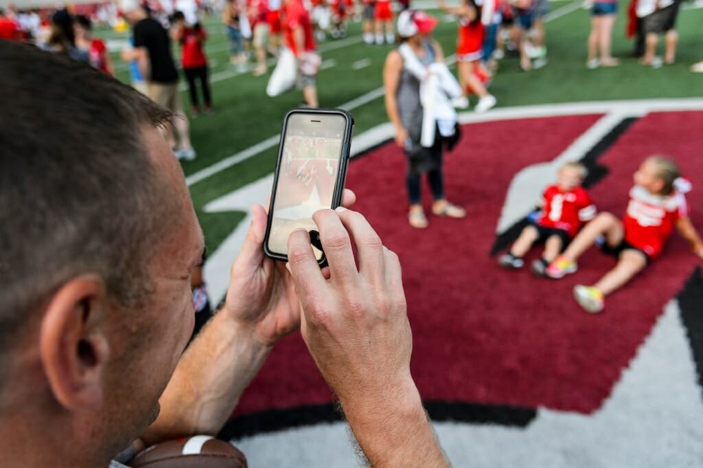 Ryan Koch takes a picture of his children Mason, 4, and Kaylie, 8, sitting on the motion W logo at center field during Football Family Fun Day at Camp Randall Stadium on Aug. 1.
