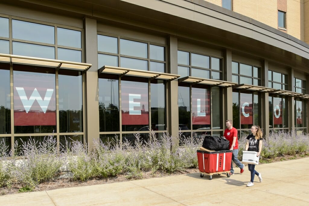 Photo: Student pushing red laundry cart in front of large building windows