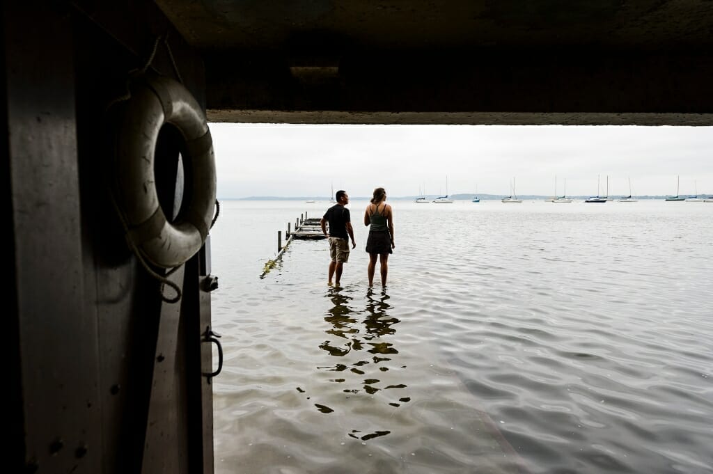 Two people stand in water and look out on a swollen Lake Mendota.