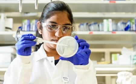 Photo: Molugu in blue gloves and white coat aiming pipette at lab dish