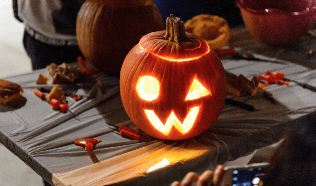 A pumpkin, with a circle and triangle for eyes and a "W" for a mouth, sits on a workstation, glowing from within. 