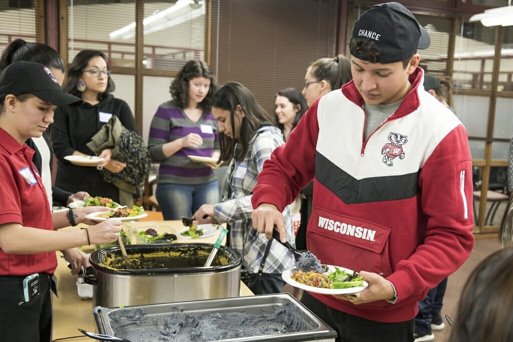 A line of students works there way down the food table, filling their plates.