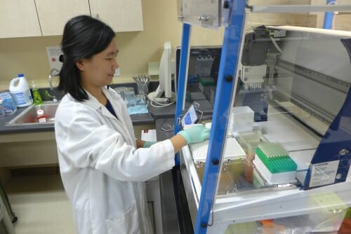 Photo: Woman in white lab coat and gloves in lab
