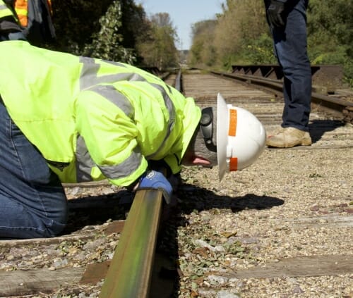 Photo: Worker in hardhat crouching and looking down track