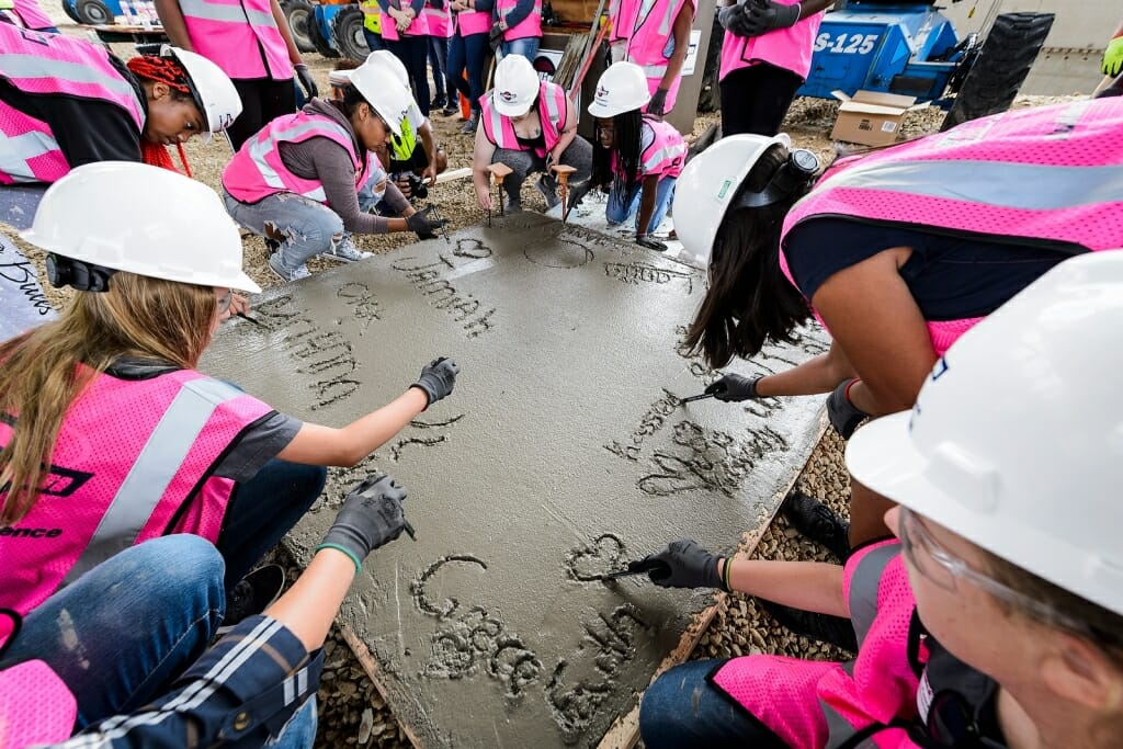 Photo: Girls in pink vests writing initials in wet cement