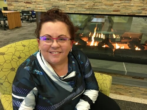 A photo of a woman in front of a fireplace. She's smiling.