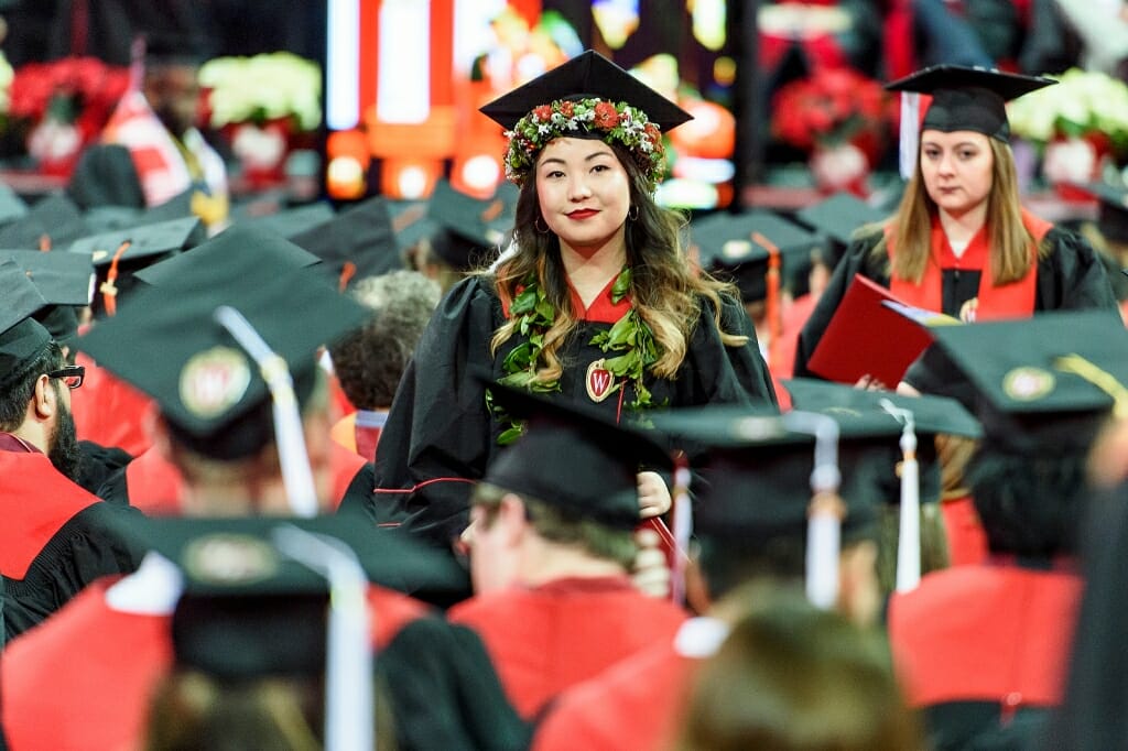 Photo of a graduate wearing a wreath of red and white flowers and greenery.