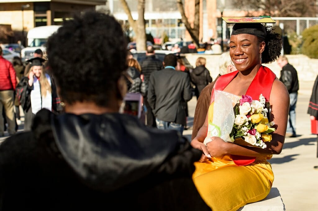 Photo of graduate Ebony McClendon, holding a bouquet of roses, posing for a photo outdoors after the ceremony.