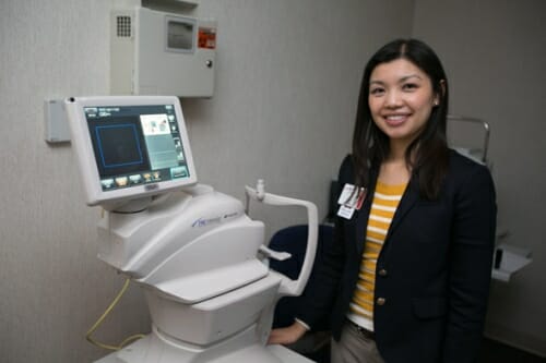 Photo of a woman next to a teleopththalmology machine. She's smiling.