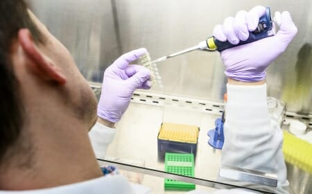 Photo: Person in rubber gloves putting something from a pipette into a vial