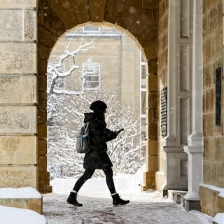 Photo: A student walking through a stone archway.