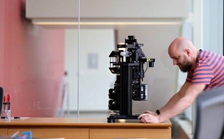 Photo of Morgridge Postdoctoral Fellow Rory Power inspecting the first iteration of the Flamingo microscope, which at a little over 40 pounds can be mailed to biology labs around the globe.