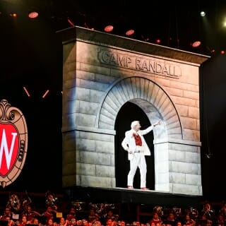 Band director Mike Leckrone stands in a model of the Camp Randall Arch as it's lowered to the stage at the start of the concert.