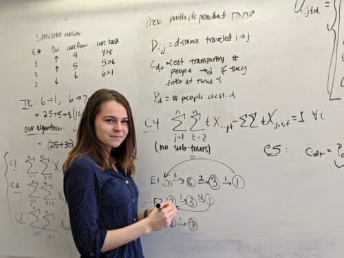 Photo: Flanigan standing in front of whiteboard with equation(s) written on it