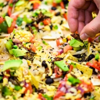 Photo: A dish of nachos, with a hand adding ingredients.