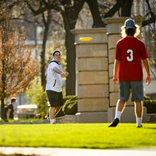 Photo: One student prepares to throw the frisbee as another waits to receive, as they stand on green grass.