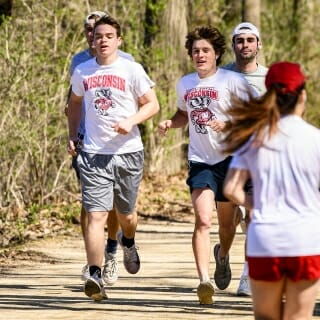 Photo: Several students jog on the gravel path, with budding trees in the background.