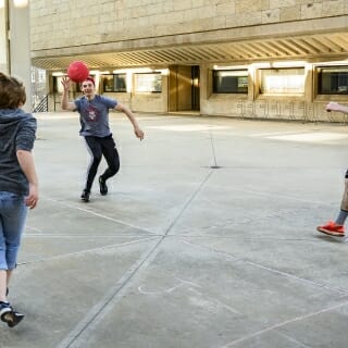 Photo: Three students play with a ball on a concrete surface.