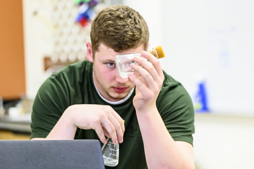 Photo: A student stares into a glass canister with liquid inside.