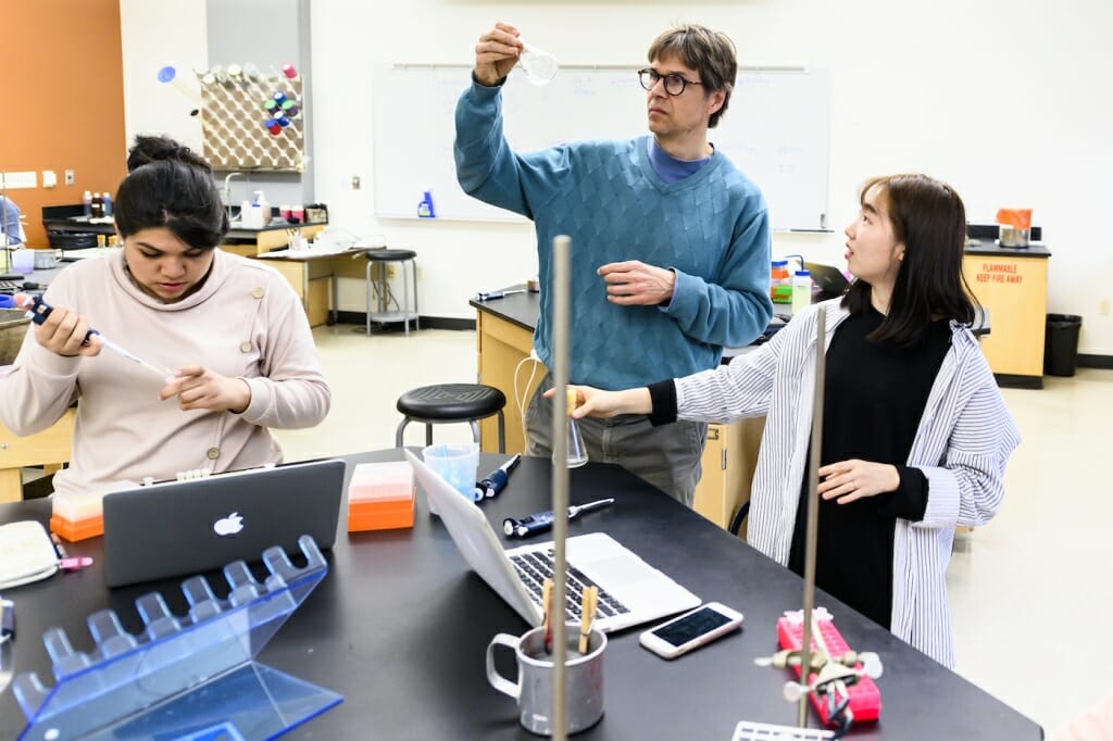 Photo: Two students and an instructor gather at a lab bench.