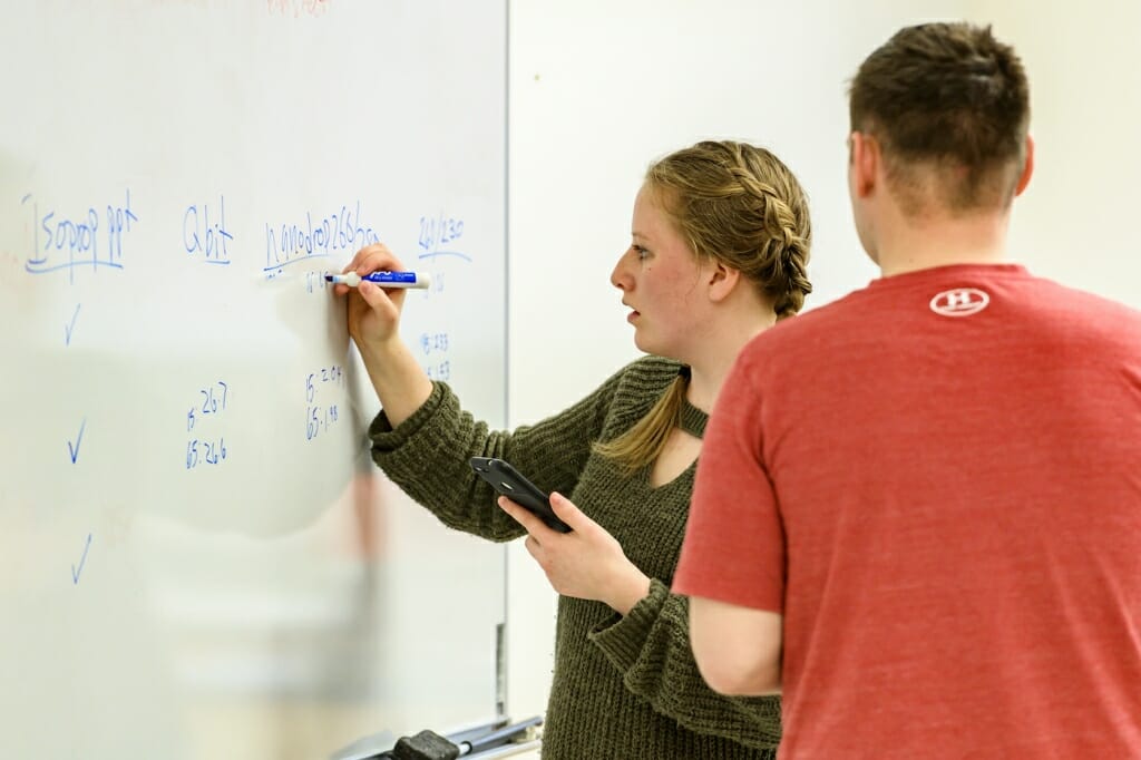 Photo: A woman writes numbers on a whiteboard.